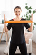 © Admiral - Smile woman exercising with latex resistance band in living room. Workout at home with fitnessband