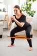 © Admiral - Sporty woman exercising with latex resistance band in living room. Workout at home with fitnessband