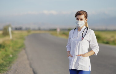 Female doctor or nurse wearing a protective face mask next to a rural road.