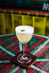 Wall Mural - A classic yellow sour cocktail with foam in a nick and nora glass with lime zest garnish