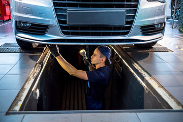 Wall Mural - Car mechanic examining car suspension of lifted automobile at service station