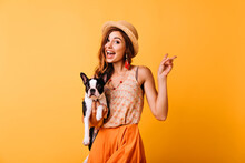 Charming Red-haired Girl In Vintage Hat Holding French Bulldog. Indoor Photo Of Amazed White Woman Posing On Yellow Background With Puppy.