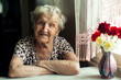Portrait of an old woman pensioner sitting at kitchen in her home.