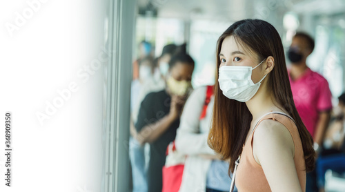 Young Asian woman passenger wearing surgical mask and waiting bus at station with crowned people when traveling in big city at Covid outbreak, Infection and Pandemic concept