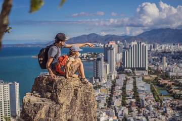 Wall Mural - Father and son local tourist sits on a rock and enjoys the view of her city. Local tourism concept. Tourism after COVID 19