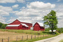 Beautiful Red Barns With Gleaming Metal Roofs Stand On A Farm Under A Cloudy Blue Sky In This Bucolic Country Scene In Rural Indiana.