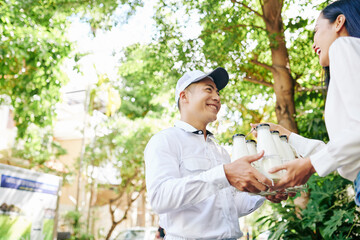 Wall Mural - Happy smiling Vietnamese delivery man giving set of milk bottles to pretty young woman