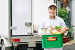 © DragonImages - Portrait of positive young Vietnamese courier holding plastic box with fresh fruits, bread and bottled milk