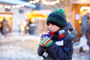 Wall Mural - Little cute kid boy drinking hot children punch or chocolate on German Christmas market. Happy child on traditional family market in Germany, Laughing boy in colorful winter clothes