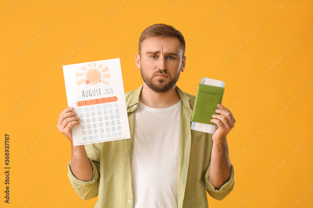 Young man with calendar, passport and ticket on color background
