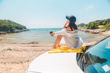 Wall Mural - woman sitting at car hood drinking coffee enjoying view of the sea