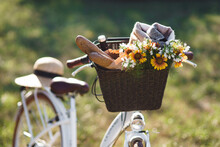 Wicker Basket With Bread Baguette, Flowers And A Picnic Blanket In A Park On A Sunny Day