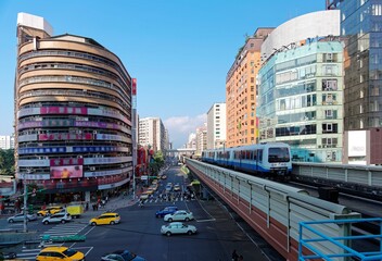 Wall Mural - Cityscape of Downtown Taipei, the capital city of Taiwan, under blue clear sky with view of busy traffic on the street and a metro train on elevated tracks of Taipei MRT System between office towers