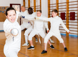 Young positive female training attack movements with rapier at fencing workout