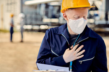 Albino construction worker with face mask holding his chest in pain while working outdoors.