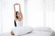 © torsakh - a beautiful Asian woman wake up and sitting on white bed in the bedroom, sexy girl stretching arms for relaxing in the morning