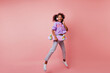 © Look! - Full-length shot of stunning black woman in stylish jeans jumping on pink background. Attractive curly african girl with skateboard expressing positive emotions.