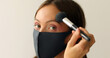 Woman in protective mask is making make-up and looking at camera on a white background