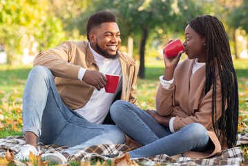 Sticker - Afro couple dating in autumn park, having picnic and drinking tea