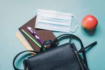 School backpack, notebook, pen, pencil, ruler, disposable mask and red apple on a green background. Coronavirus COVID-19 safety regulations an educational institution