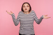 Don't know, whatever! Portrait of confused woman in striped sweatshirt shrugging shoulders in doubts, not sure and uncertain about difficult question. indoor studio shot isolated on pink background