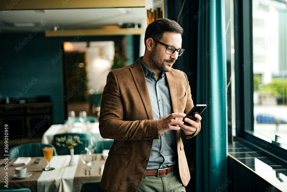 Handsome businessman standing near the window in the restaurant, using ...