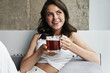 Image of beautiful joyful woman drinking tea while resting on couch