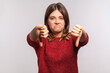 © khosrork - Awful service! Portrait of displeased girl in shaggy sweater showing double thumbs down and grimacing with disgust, expressing disapproval, bad feedback. indoor studio shot isolated on gray background