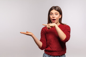 Wall Mural - Wow, attention at advertisement! Portrait of surprised shocked girl pointing at empty space on her palm, blank wall for commercial idea, product image. indoor studio shot isolated on gray background