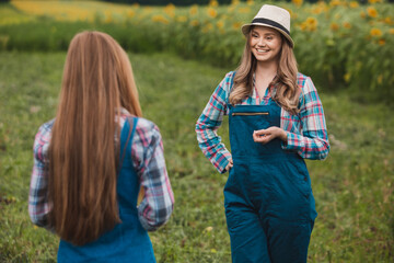 Two beautiful farmerettes having a discussion in the middle of a blooming sunflower field.