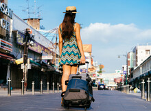 Rear View Of Young Hispanic Brunette Woman On Vacation With Luggage On Pedestrianised Street