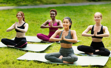 Wall Mural - Wellness concept. Tranquil young women deep in meditation during their morning yoga class in nature