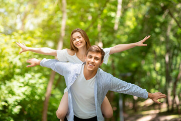 Young loving coupe at park. Boyfriend carrying his girlfriend on his back outside