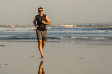 jogging Summer workout - young attractive and fit runner man training on beautiful beach running barefoot free and happy by the sea in fitness and healthy lifestyle concept