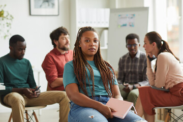 Wall Mural - Multi-ethnic group of people sitting in circle while discussing business project in office, focus on African-American woman looking at camera in foreground, copy space