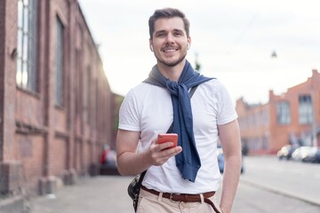 Canvas Print - Handsome smiling man listening to music while walking in the city.