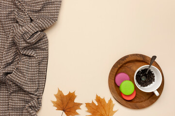 Wall Mural - Flat lay autumn composition. White cup with tea leaves, wooden plate, knitted fashion sweater or plaid, pants in a pattern, yellow maple leaves cinnamon orange on beige background top view copy space