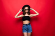 © dianagrytsku - Young pretty woman in floppy hat and sunglasses standing isolated on red background