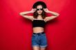 © dianagrytsku - Young pretty woman wearing sunglasses and floppy hat isolated on red background