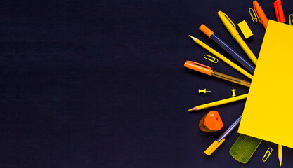 The concept of going back to school. Yellow-orange school supplies, notebooks, pencils, pens, paper clips, buttons on a black background. Space for text