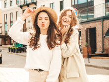 Two Young Beautiful Smiling Hipster Girls In Trendy White Sweater And Coat. Sexy Carefree Women Posing On Street Background In Hat. Positive Models Having Fun, Going Crazy And Make Duck Face