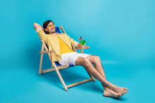 Full Size Photo Positive Guy Enjoy Rest Relax Exotic Resort Sun Bathing Hold Glass Cocktail Sit Deckchair Wear White Yellow Striped Shirt Shorts Barefoot Isolated Blue Color Background