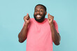 © ViDi Studio - Excited young african american man guy in casual pink t-shirt posing isolated on blue background studio portrait. People lifestyle concept. Mock up copy space. Wait for special moment clenching fists.