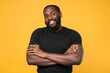 © ViDi Studio - Smiling african american man guy football fan in casual black t-shirt isolated on yellow background studio portrait. People sincere emotions lifestyle concept. Mock up copy space. Hold hands crossed.