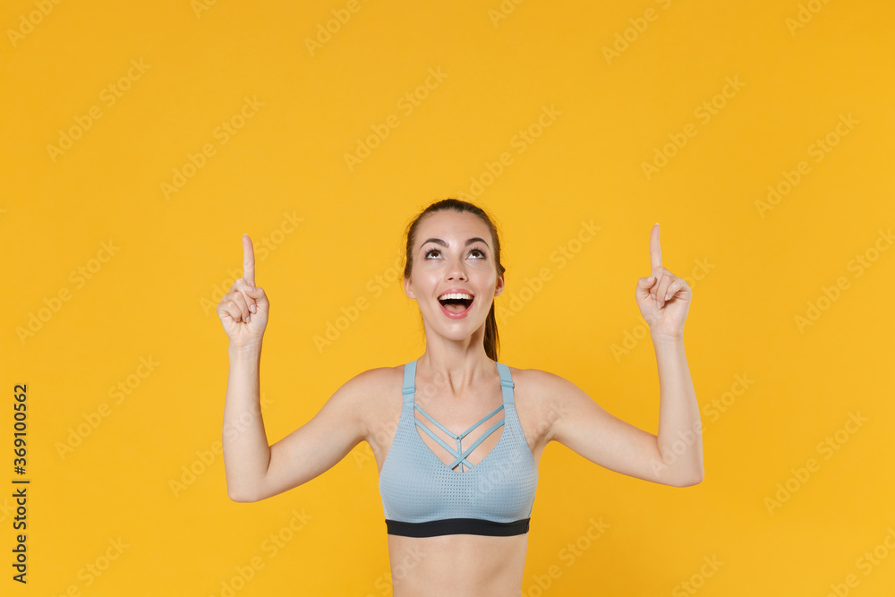 Excited young fitness sporty woman girl in sportswear working out isolated on yellow wall background studio. Workout sport motivation lifestyle concept. Mock up copy space. Pointing index fingers up. - obrazy, fototapety, plakaty 