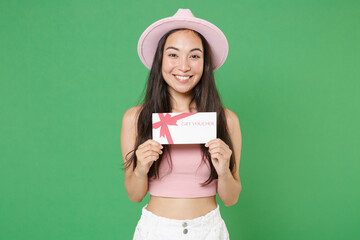 Wall Mural - Smiling young asian woman girl in casual pink clothes hat posing isolated on green background studio portrait. People sincere emotions lifestyle concept. Mock up copy space. Hold gift certificate.