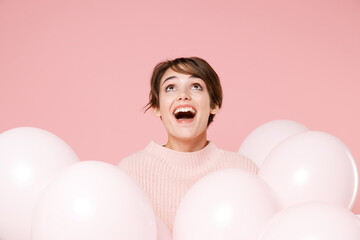 Surprised young brunette woman girl in knitted casual sweater posing isolated on pastel pink background. Birthday holiday party, people emotions concept. Celebrating hold air balloons. Looking up.