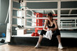 © Sibstock/Stocksy - young attractive girl tired after boxing training, sitting in the ring. dark boxing gym with a ring