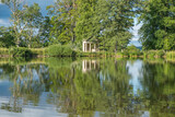 Fototapeta Na ścianę - A view across a beautiful lake with reflections of trees towards an old abandoned structure in the middle of a rural countryside scene