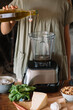 © Alberto Bogo/Stocksy - Woman pouring olive oil into professional blender for preparing pesto
